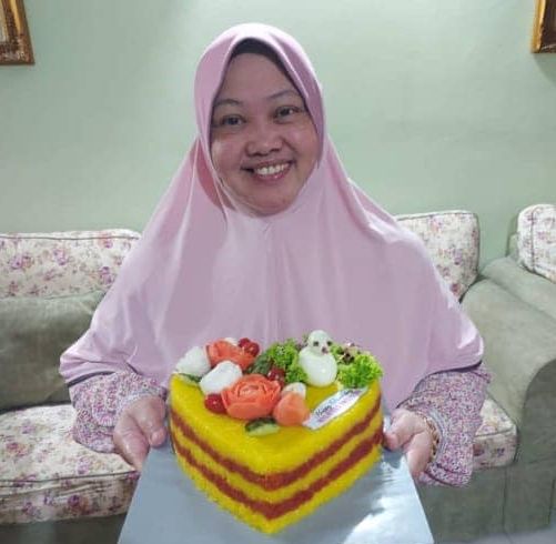 Norhayati Tajuddin smiles as she holds a pulut kuning cake. 