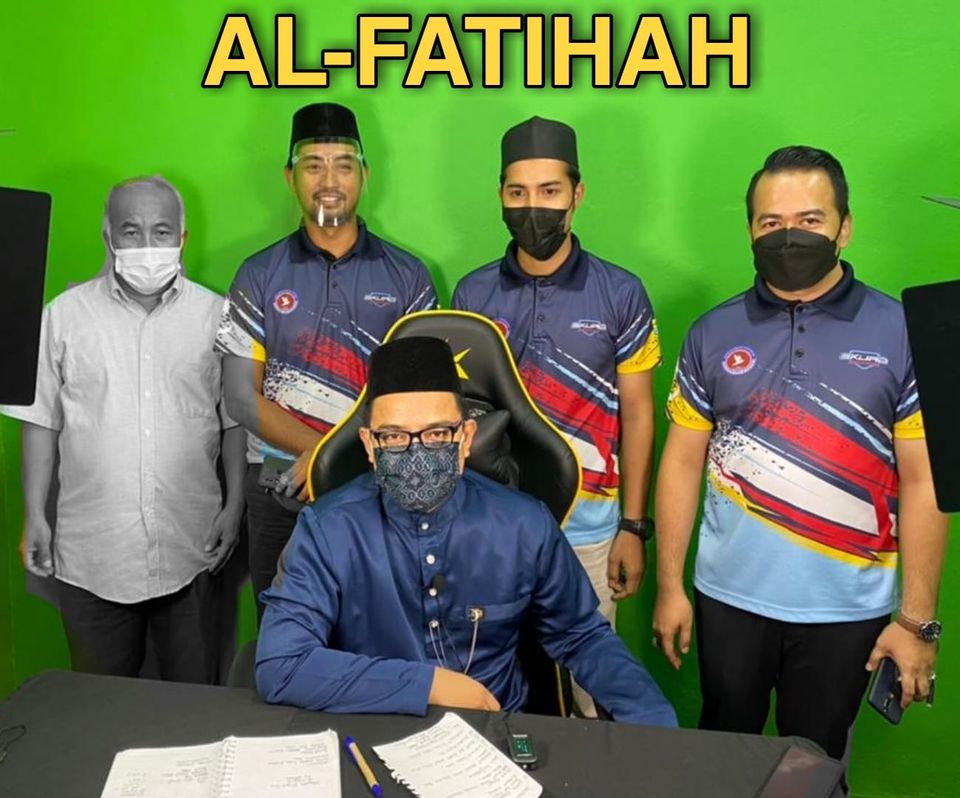 Ramli bin Ibrahim stads next to three colleagues, behind another collague who is sat. He is wearing a face mask. 
