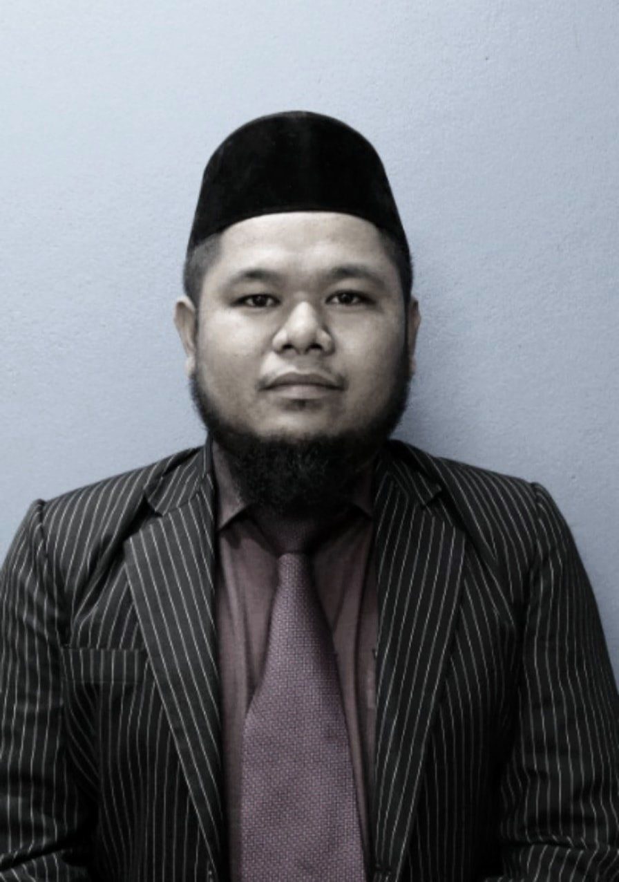 Mohd Hanif Menhad in a passport photo. He is wearing a pinstripe blazer with maroon shirt and tie and a songkok. He has a bushy black beard.