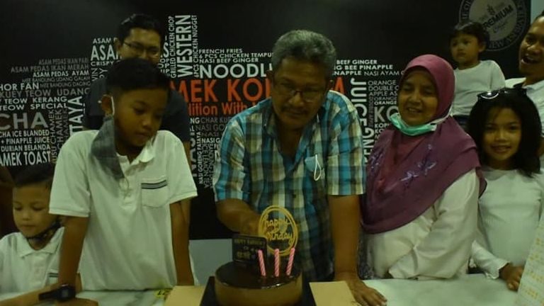 Md Yusop Talib cuts his birthday cake while surrounded by his family.