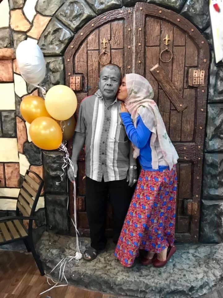 Salehuddin bin Hamid receives a kiss on the cheek from his daughter Mimi. He is holding helium baloons.