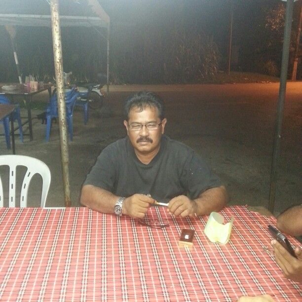 Zulkifli Bakri squints at the camera as he sits at a food stall. He has tanned skin, thinning floppy hair and a mustache.