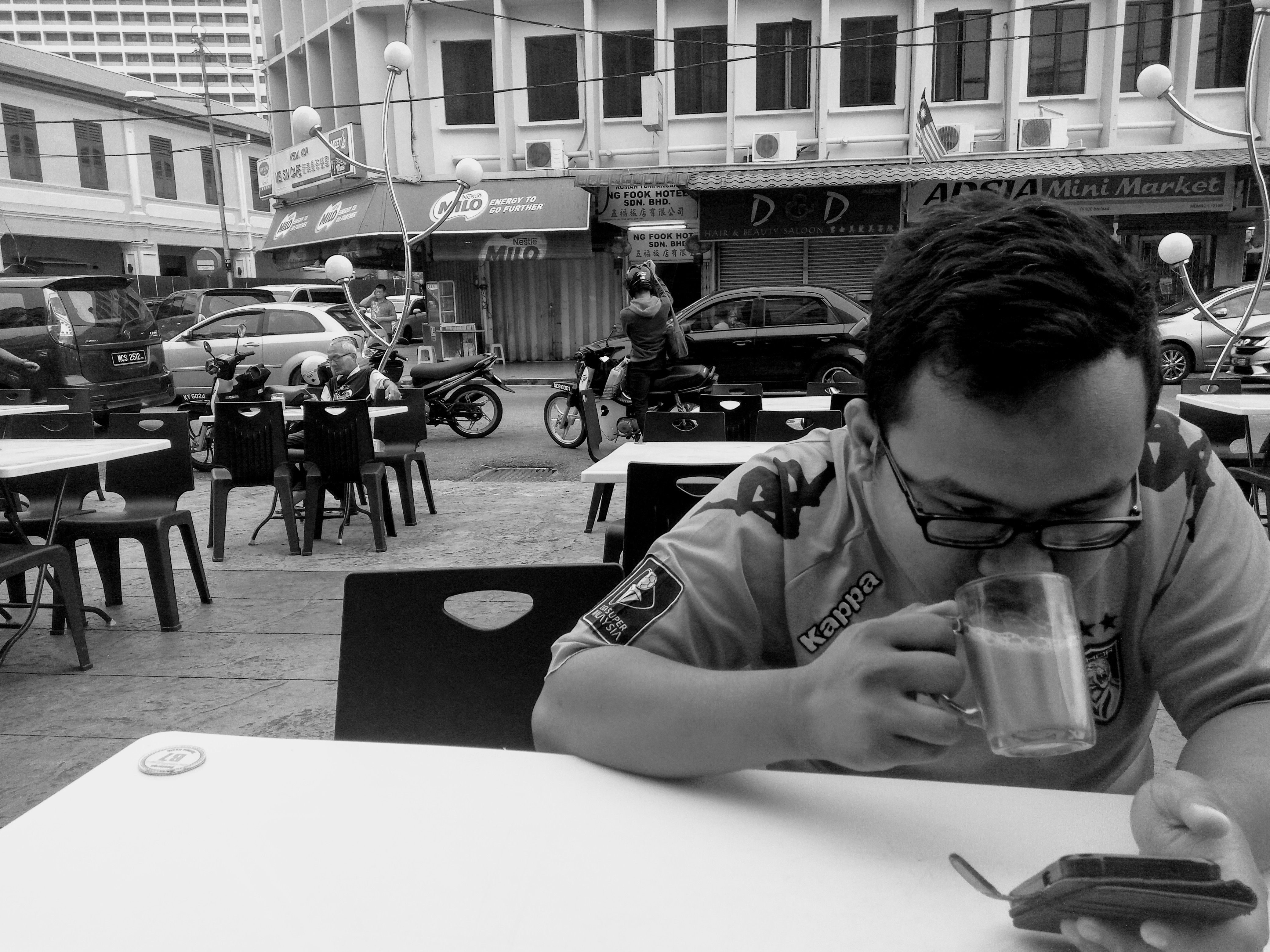 Aliff Hanif Ehsan, aged 26, drinking teh tarik and scrolling through his phone at an eatery. 