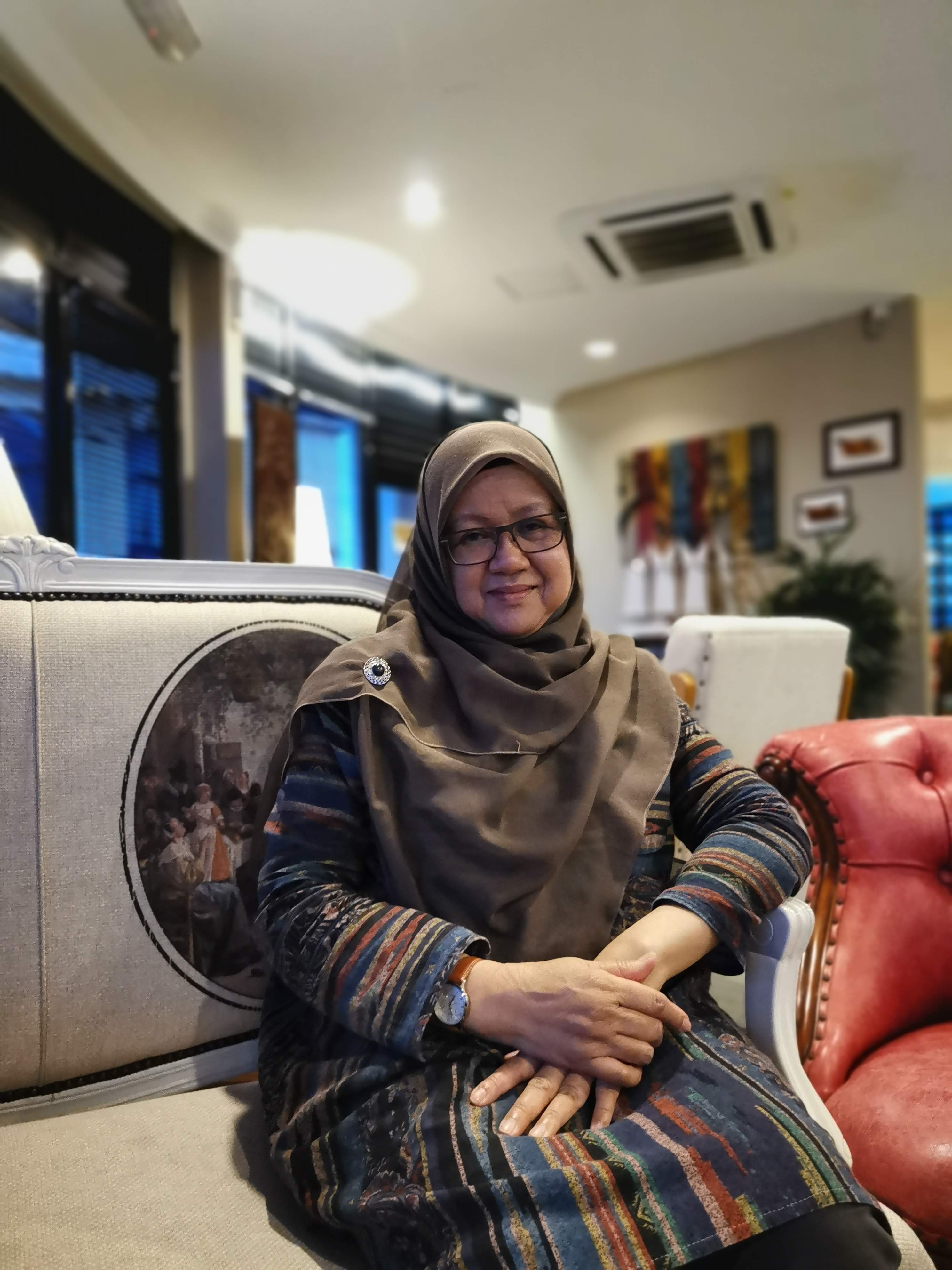 Khamsiah Binti Ismail posing at home during Hari Raya. She is in a head scarf and baju kurung.