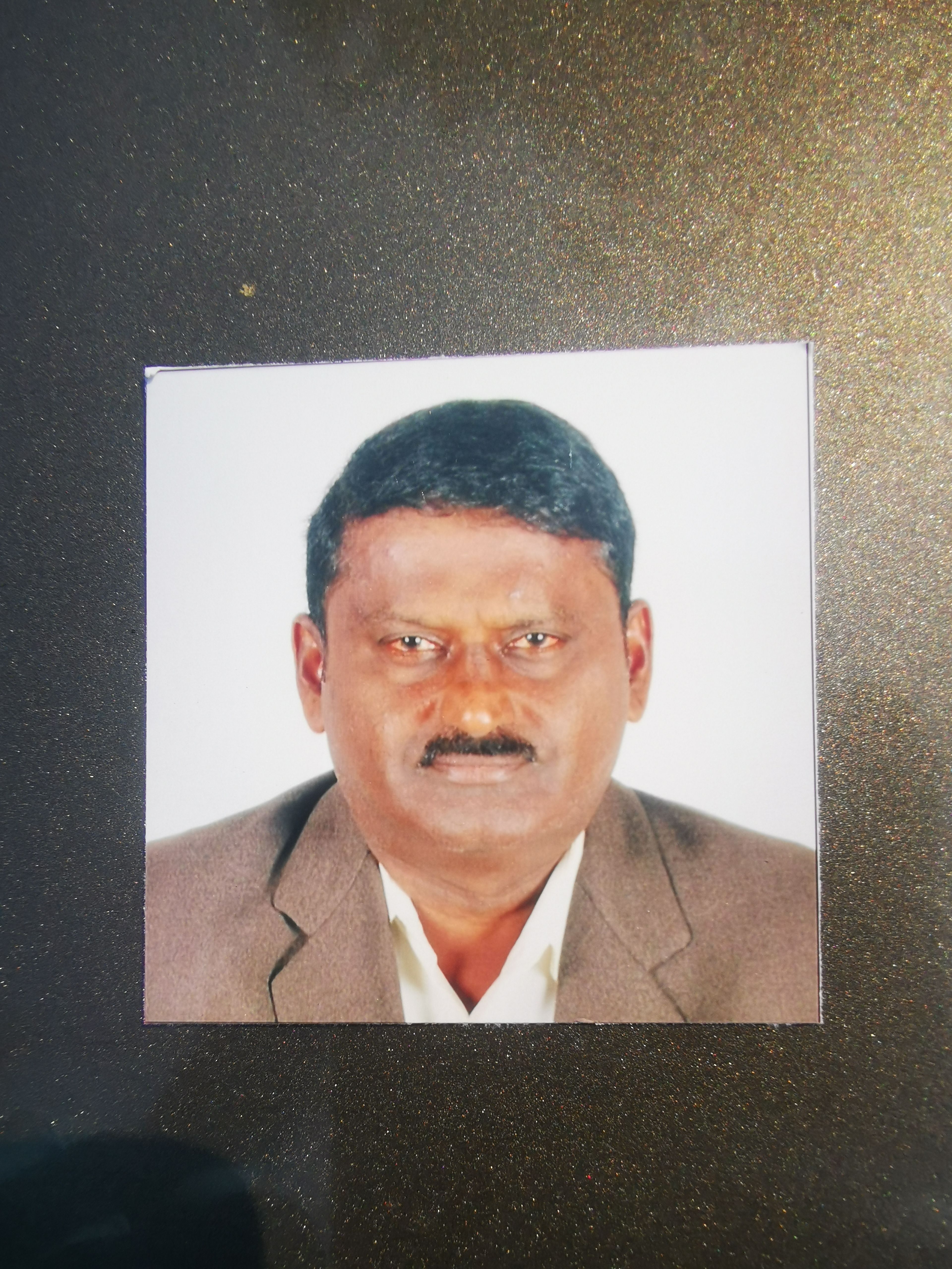 Moorthy A/L Perumal, 56, in a passport photo. He has brown skin, black short hair and a black mustache. He is wearing a brown jacket and a white shirt.