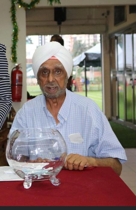 Jeswant Singh, 73, has tanned skin, and grey mustache, beard and eyebrows. He is wearing a white turban and a blue and white short-sleeved cotton shirt. 