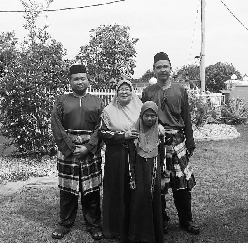 A  family potrait of Fatimah Mustafa, her husband Yes, husband, Juhari Ibrahim,  son Muhammad Syukri Juhari and young daughter. They are in baju kurung and baju melayu and posing on a front lawn. .