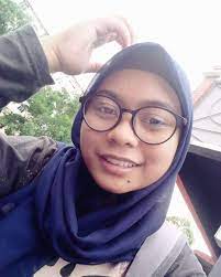 Nurul Atikah wears dark-rimmed large-framed glasses. She smiles for the camera.