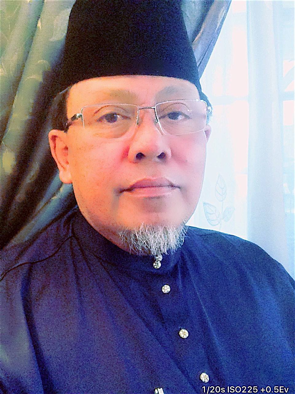 Che Nazran Haji Abdullah in baju melayu and songkok. He wears rimless glasses and has a white goatee.