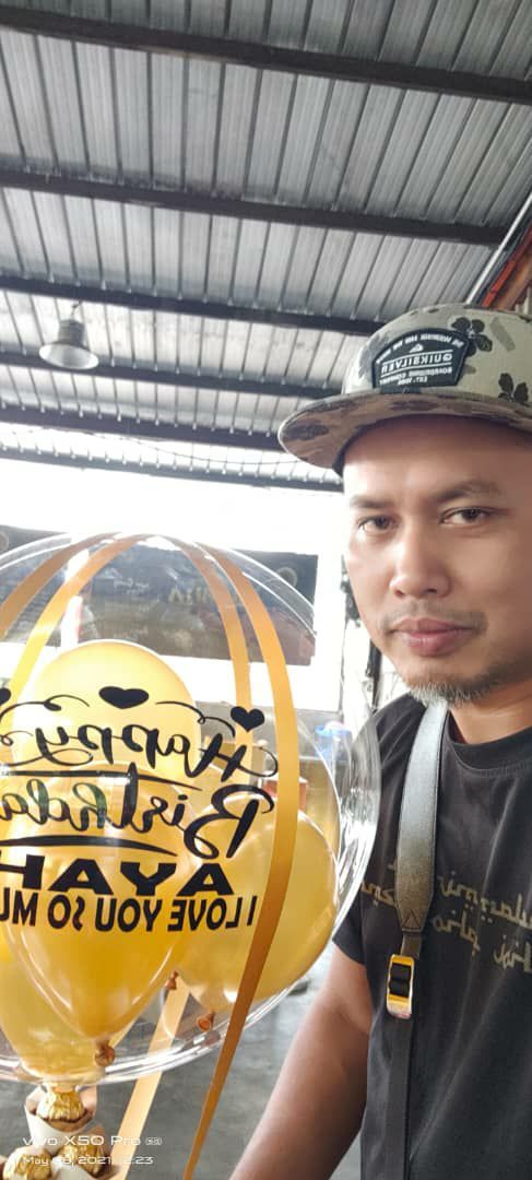 Saifoldin Sulaiman, 47, has brown skin, a goatee and thin mustache. He wears a cap and black T-shirt and holds a balloon which reads: Happy Birthday, Ayah. I love you so much.